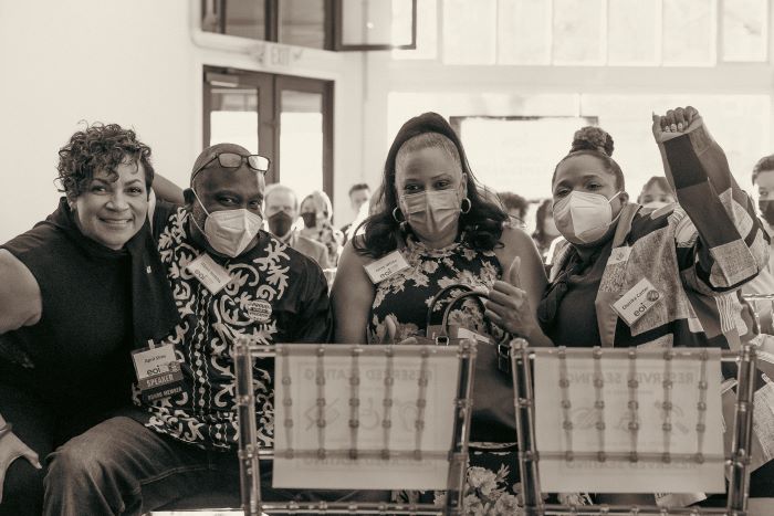 Photo of group of people smiling and masked. One person has their fist up in solidarity.