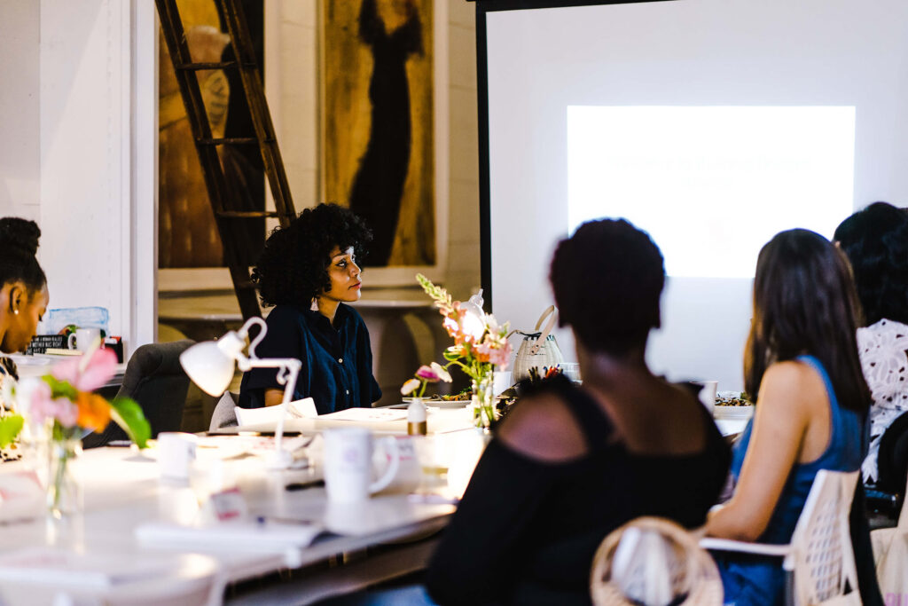 Black Women In Workplace, sitting at a conference table looking at a presentation on the screen